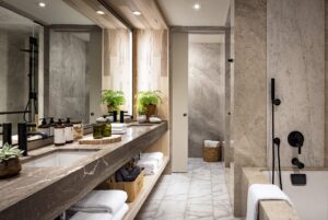A modern bathroom with double vanity, black fixtures, light stone walls, and a separate tub and shower area.
