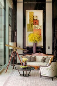 Ornate sitting area featuring an antique-style settee, a glass coffee table, and an embroidered armchair. A brass telescope stands by tall windows.