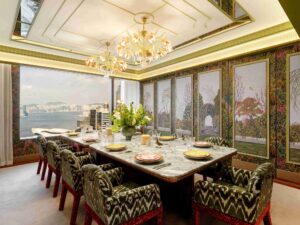 Formal dining room overlooking a harbor. Features a large veined marble table, ten patterned chairs, and ornate ceiling and wall details.