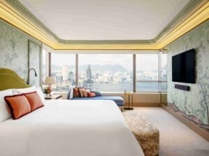 Bedroom with sage Chinoiserie wallpaper, king bed, and blue velvet chaise lounge looking out onto a panoramic cityscape and harbor.