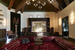 Sunken living room with a red leather U-shaped sectional facing a dark wood entertainment center. Features a vaulted ceiling and high-end audio speakers.