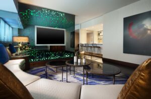 Modern living room with a segmented sofa, three round coffee tables, a large TV on a green-patterned wall, and a bar with stools.