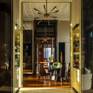 View into a formal dining room with a round pedestal table, dark leather chairs, and a starburst chandelier. Gold trim details line the entryway.
