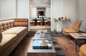 A contemporary living room with a tan sofa, an orange leather armchair, and three textured metallic coffee tables near a rolling bar cart.