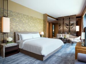 A modern bedroom with a large bed, sitting area, decorative gold-patterned wall, and blue abstract patterned carpet.