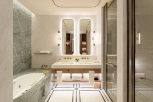 A luxurious marble bathroom features a double vanity with backlit mirrors, a large built-in bathtub, and a glass shower.