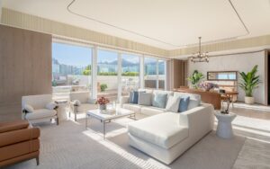 A bright modern living room with a large sofa, armchairs, and a coffee table. Floor-to-ceiling windows overlook a terrace.