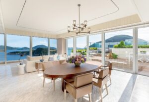 Modern living and dining room with floor-to-ceiling windows, ocean views, and an outdoor terrace with seating.