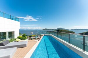 An outdoor plunge pool on a wooden deck with lounge furniture, overlooking a blue ocean with green islands.