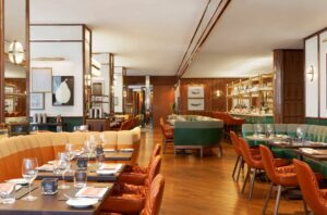 A lively restaurant with orange and green seating, dark wood tables, and a full bar area in the background.
