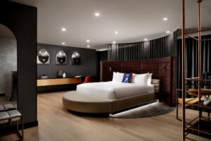 Modern bedroom with a circular bed, curved velvet headboard, light wood floor, and dark accent wall.