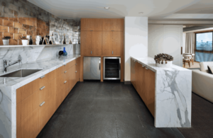 Galley kitchenette with wood cabinets, dramatic marble counters, a sink, integrated refrigerator, and wine cooler on a dark tiled floor.