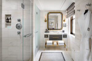 Modern bathroom with white marble-patterned tiles, a glass shower, a vanity, a geometric mirror, and a window.