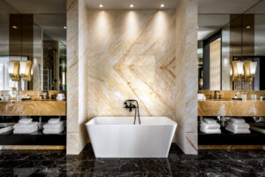 A luxurious bathroom with a white freestanding tub, dual light marble vanities, black faucets, and dark marble floors.