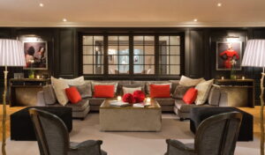 A sophisticated living room with a large gray sectional sofa, red pillows, a square coffee table, and dark paneled walls with art.