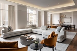 A modern living and dining room with a white sectional sofa, round coffee tables, and a long dining table under a geometric chandelier.