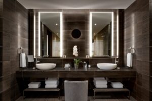 Modern bathroom double vanity with dark stone walls and countertop, two white basin sinks, and illuminated mirrors.