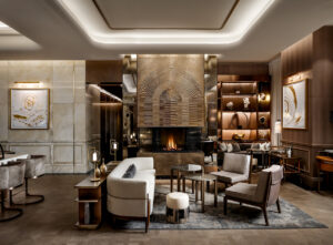 Modern living area centered on a fireplace with a large radial bronze-toned metal screen. Seating includes an off-white sofa and two taupe armchairs.