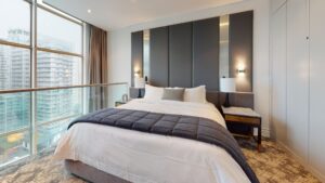 Modern bedroom with a large bed, dark headboard, two nightstands, lamps, and floor-to-ceiling city view windows.